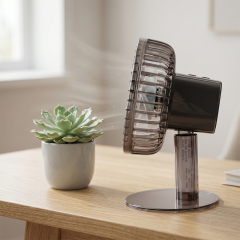 Side view of a portable rechargeable table fan blowing air next to a small succulent plant pot on a wooden coffee table