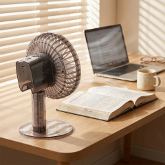 Rear side view of a translucent oscillating desk fan on a wooden study table next to an open book and laptop