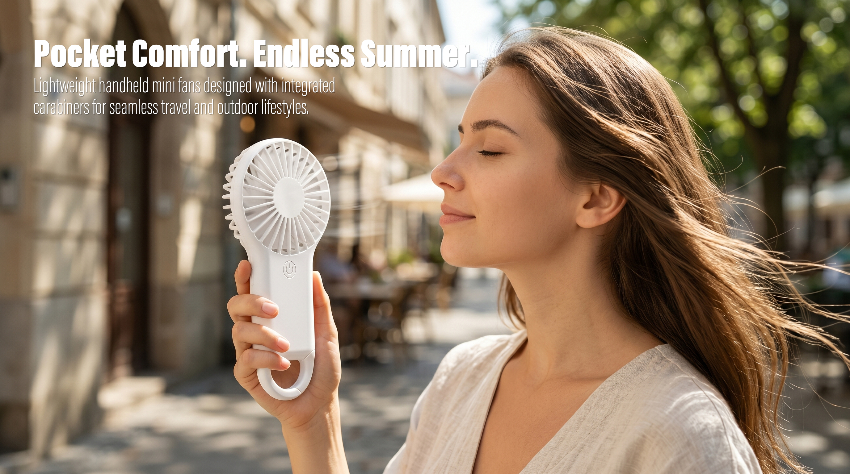 A side profile of a young woman enjoying a cool breeze from a white handheld mini fan on a sunlit city street with trees and historical buildings in the background.