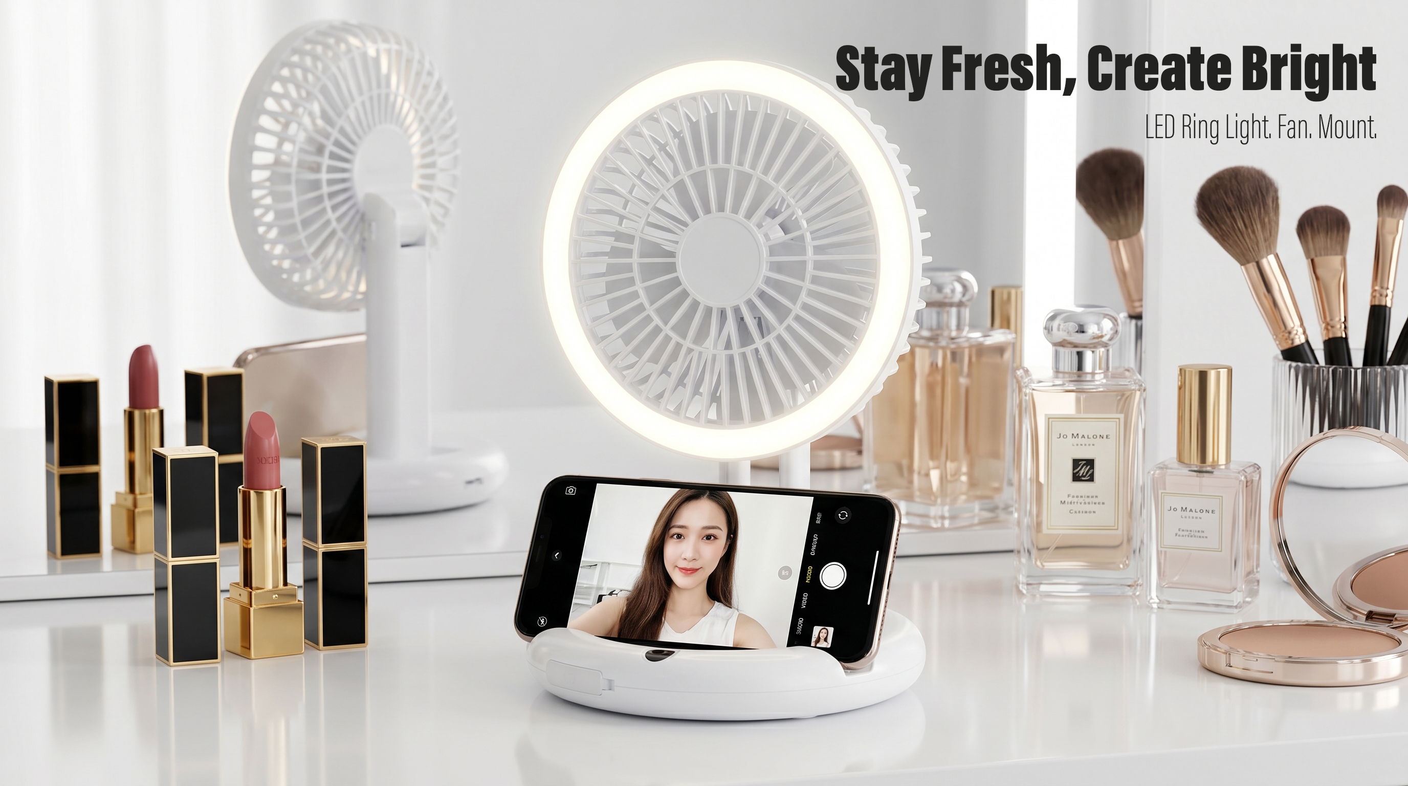 A white portable desk fan with an illuminated LED ring light and smartphone holder is presented on a white vanity table surrounded by luxury cosmetics, designed for live streaming.