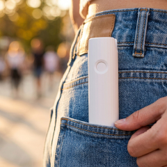 Close-up view of a person inserting the compact white telescopic mini fan into the back pocket of blue jeans.