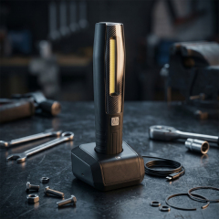 Black rechargeable LED work light standing in its charging dock on a dark workshop workbench surrounded by tools.