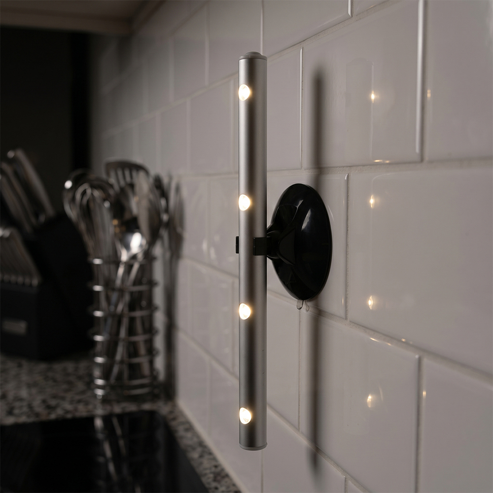 A silver LED light bar mounted vertically on a white tiled kitchen wall using a black circular magnetic base.