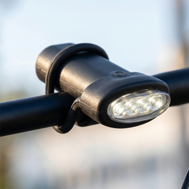 A black silicone LED bicycle light securely mounted on a black metal handlebar using its integrated flexible strap.