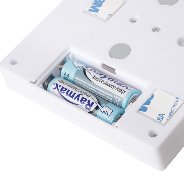 Close-up studio shot of the opened battery compartment on the back panel, showing the installed AA batteries along with the mounting magnets and adhesive strips.
