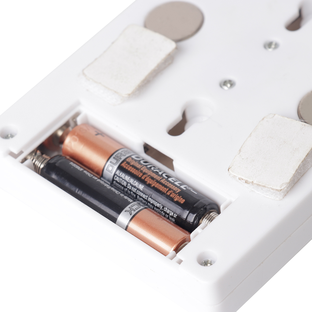Close-up view of the open battery compartment on the back panel, showing the installed AAA batteries alongside the circular mounting magnets and velcro tape.
