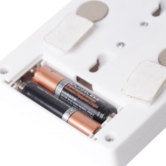 Close-up view of the open battery compartment on the back panel, showing the installed AAA batteries alongside the circular mounting magnets and velcro tape.