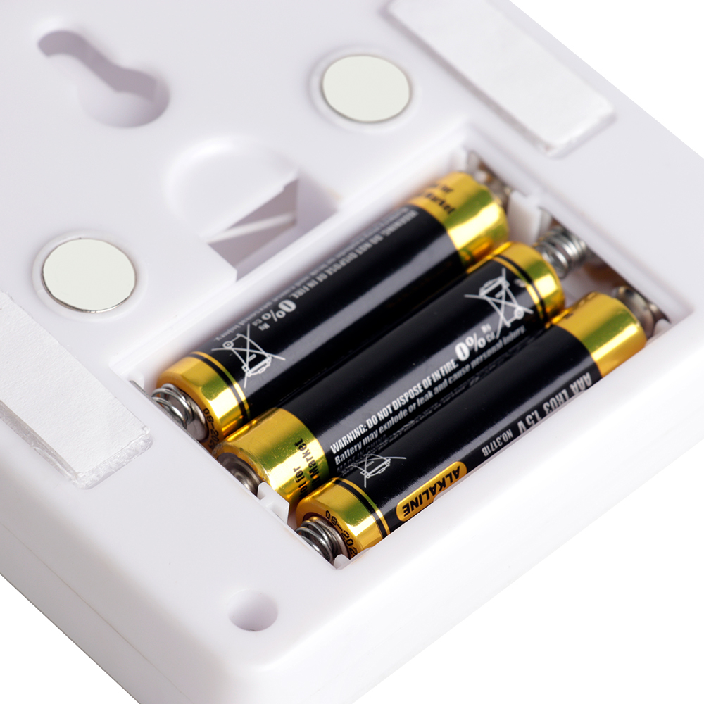 Close-up studio shot of the opened battery compartment on the back panel, showing three AAA batteries installed next to the built-in mounting magnets.