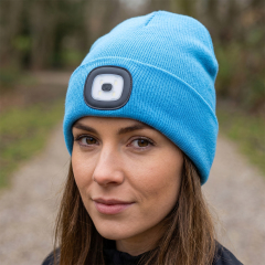 Close-up portrait of a woman outdoors wearing a vibrant blue winter beanie hat with a central rechargeable LED light.