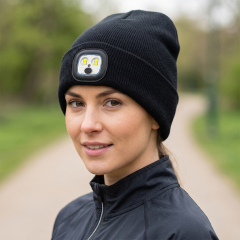 A woman wearing a black knitted beanie with a square LED module showcasing white and yellow multi-color light output options.