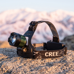 A 10W T6 LED headlamp with green cooling fins and a balanced three-strap headband, set on a rough rock with a soft-focus snowy mountain range background.