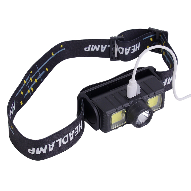 Studio top-angle view of the compact head torch with a white Micro USB charging cable connected directly into the top power port of the housing.