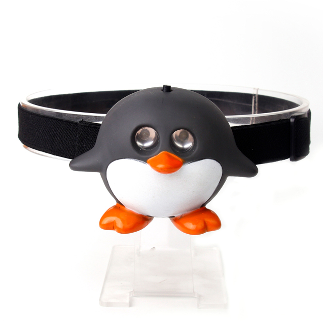 Studio front view of a custom black and white cartoon penguin-shaped kids head torch with dual glowing lenses.