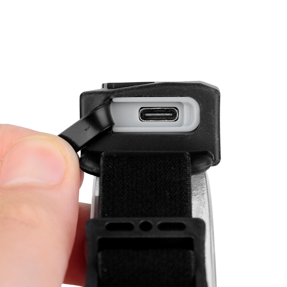 Studio close-up view of a hand pulling back a protective rubber cover to reveal the integrated Type-C USB charging port on the headlamp module.