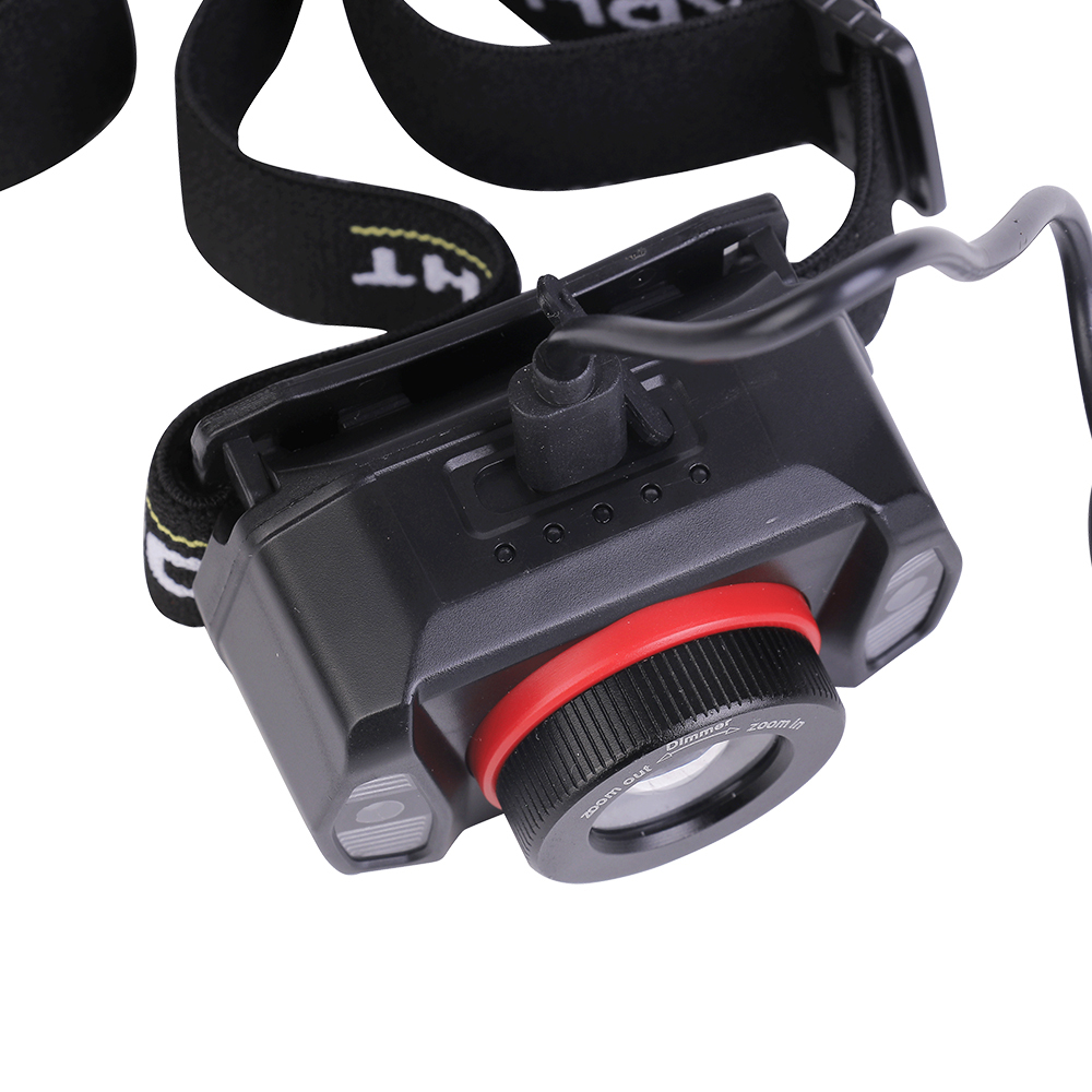 Studio close-up view of the top of the black headlamp housing, showing a cable plugged into the charging port, with the red-ringed lens module visible below.
