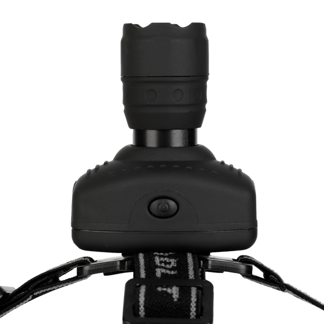 Studio top-down view of the headlamp module, highlighting the central circular push-button switch on the housing and the extension of the zoomable lens barrel.