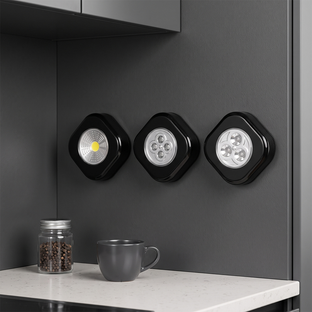 Three black rounded-square wireless LED cabinet lights mounted side-by-side on a dark gray wall above a white kitchen countertop with a mug and a coffee bean jar.
