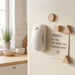 A white curved wireless LED motion sensor night light magnetically attached to the side of a white refrigerator next to a magnetic notepad in a kitchen.