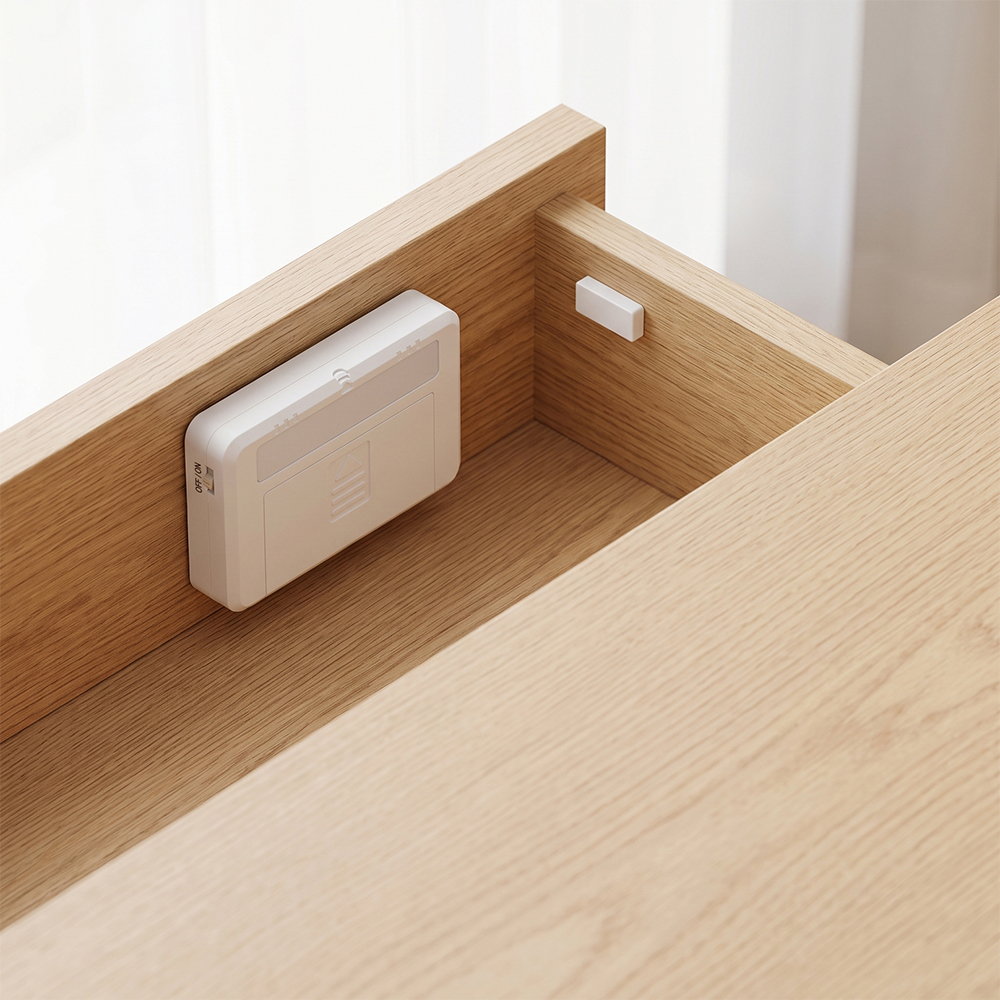 A small white wireless magnetic sensor drawer light and its contact magnet mounted inside an open wooden drawer.