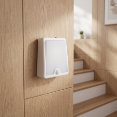 Studio view of a white square PIR motion sensor LED night light mounted on a wooden wall near an indoor residential staircase.