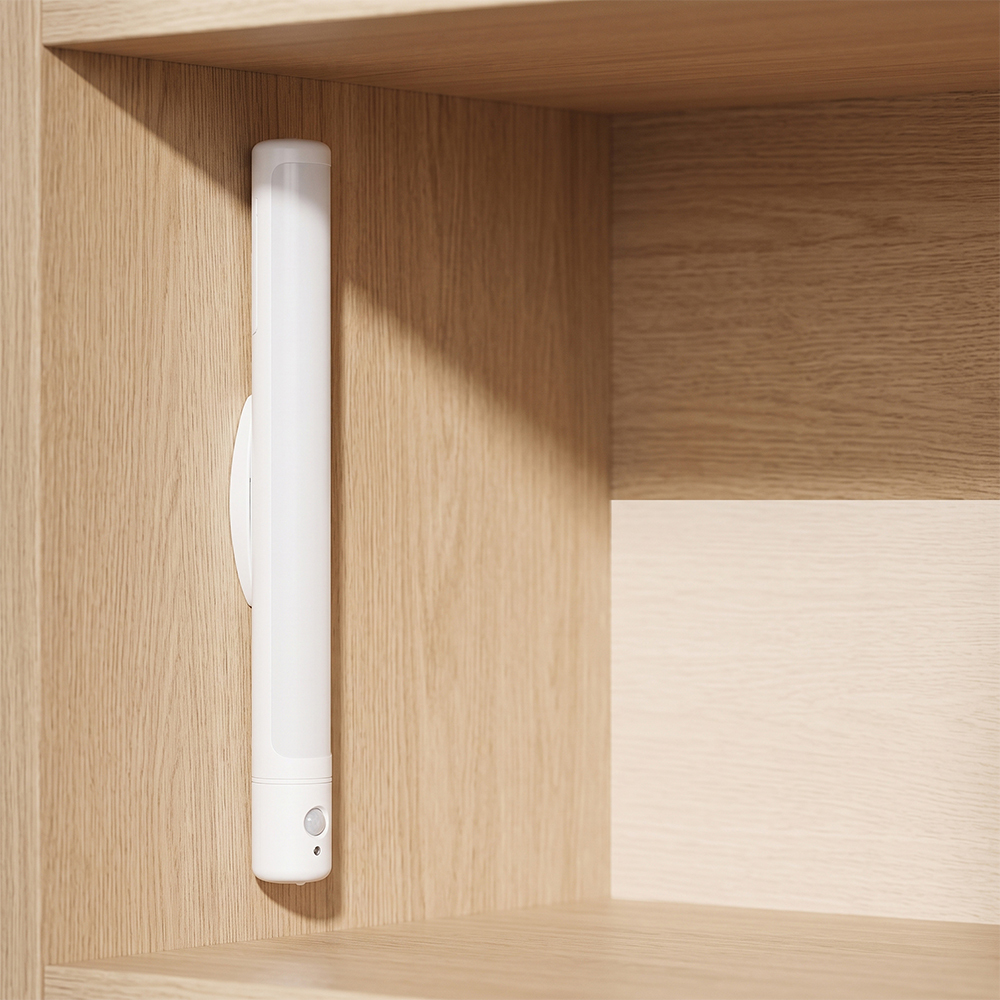 A white battery-powered PIR motion sensor LED closet light bar vertically mounted on its support stand inside a light wooden cabinet.