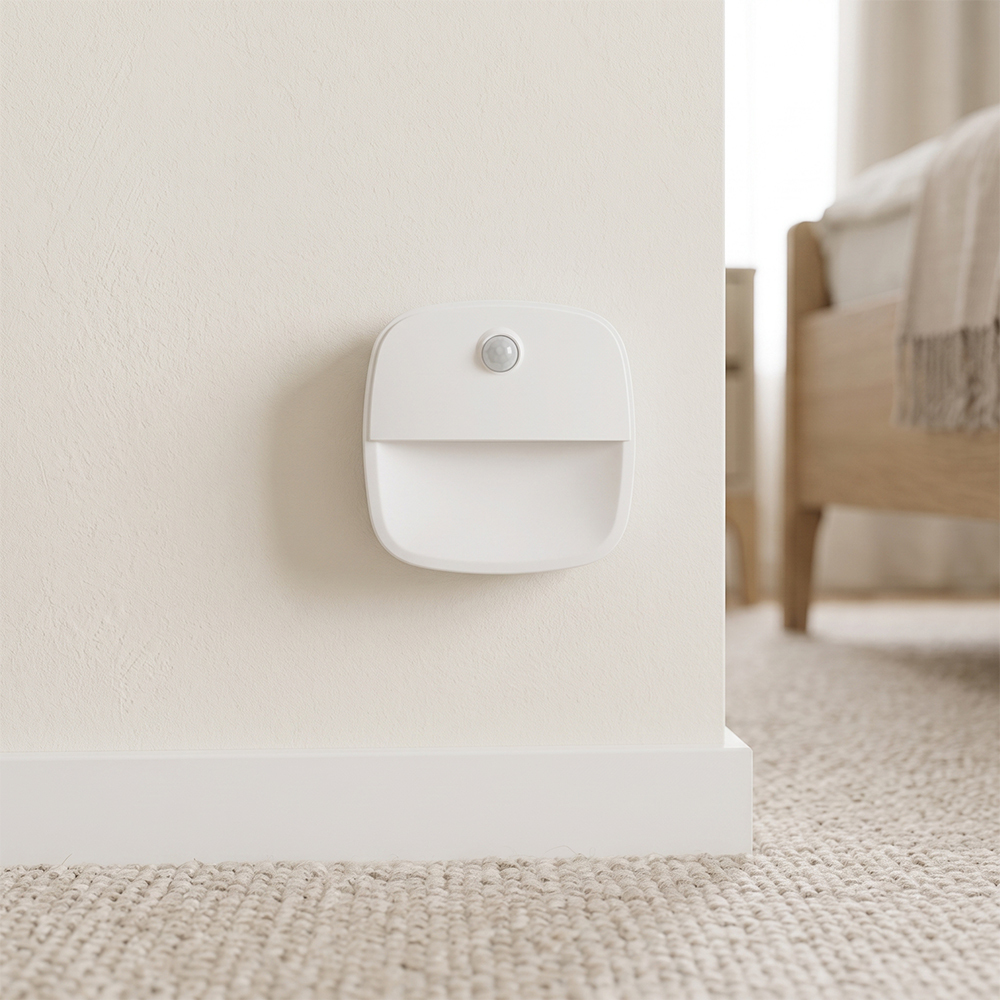 A white square PIR motion sensor LED night light mounted on a bedroom wall near the baseboard flooring.