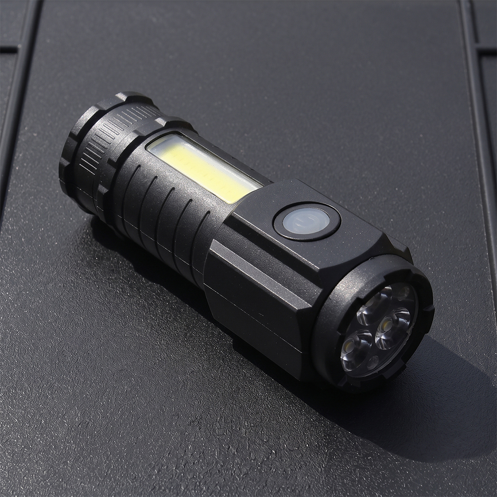 A black mini rechargeable flashlight with 3 LED front bulbs and a side COB floodlight panel lying on a dark surface.