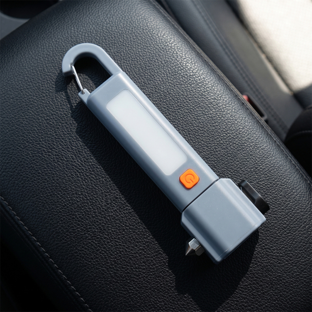 A greyish-blue multifunctional car emergency flashlight with carabiner hook lying on a black leather car seat.