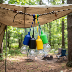 Multiple colorful LED pull cord bulb lights hanging together from a rope under a camping tarp outdoors.
