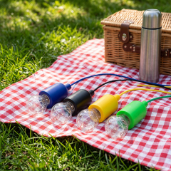 Four colorful LED pull string bulb lights laid out on a red plaid picnic mat on the grass next to a basket and thermos.
