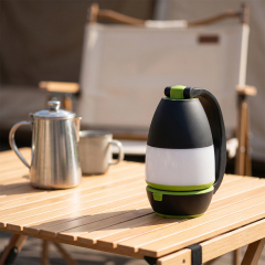 A black and green multifunctional LED camping light standing on a wooden foldable campsite table next to a kettle.