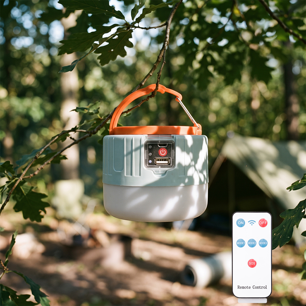 A blue and white solar camping lantern hanging from a tree branch in a campsite, with its remote control unit next to it.