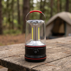 A black and red dimmable COB LED camping lantern standing on a wooden picnic table with a tent in the blurred forest background.