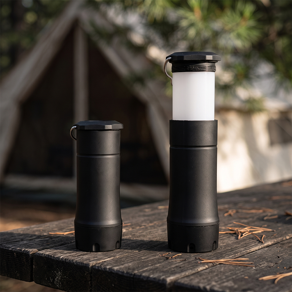 Two black telescopic LED lights placed on a wooden campsite table, showing both compact flashlight and extended lantern modes.