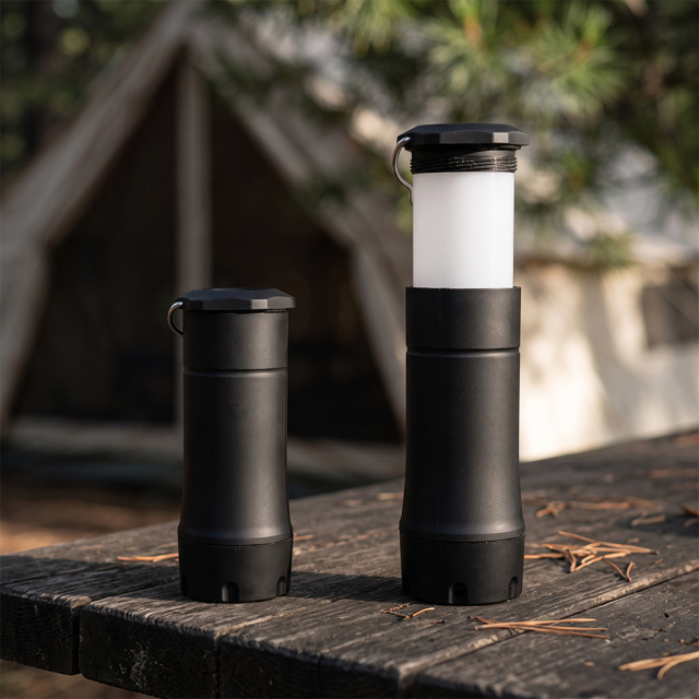 Two black telescopic LED lights placed on a wooden campsite table, showing both compact flashlight and extended lantern modes.