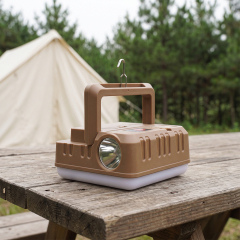 A brown multi-functional LED camping work light sitting on a wooden picnic table near a campsite tent.