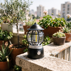 A black vintage COB LED camping lantern sitting on a stone patio ledge surrounded by potted plants.