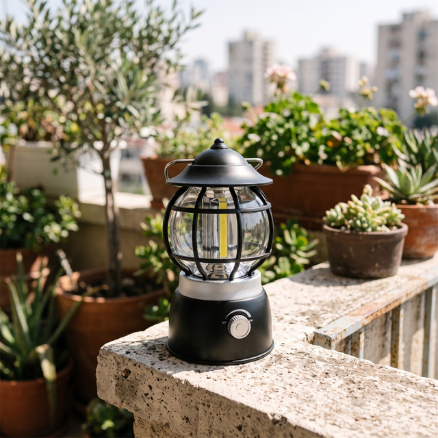 A black vintage COB LED camping lantern sitting on a stone patio ledge surrounded by potted plants.