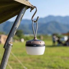 A mini portable LED tent light hanging from an S-hook on a camping tent pole outdoors.
