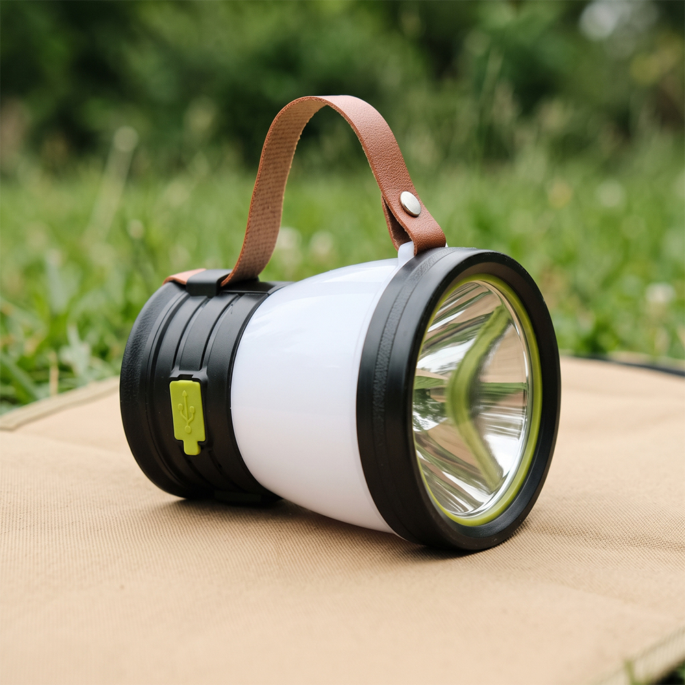 A solar LED camping lantern with a leather strap resting on a mat outdoors on the grass.