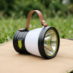 A solar LED camping lantern with a leather strap resting on a mat outdoors on the grass.
