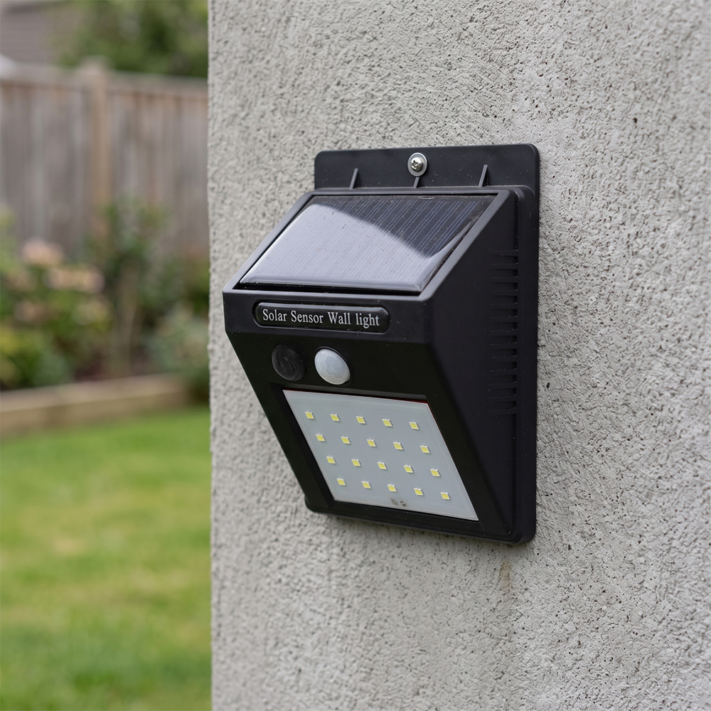 A black solar motion sensor outdoor wall light mounted on a concrete wall in a garden.