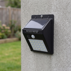 A black solar motion sensor outdoor wall light mounted on a concrete wall in a garden.