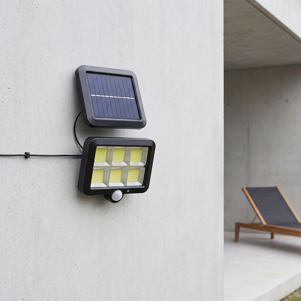 A split solar motion sensor outdoor light with a separate solar panel mounted on a concrete wall in a modern patio.