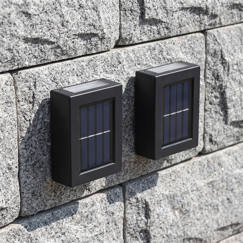 Two black compact solar up and down wall lights mounted on a textured grey stone wall in daytime.