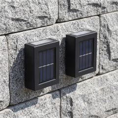 Two black compact solar up and down wall lights mounted on a textured grey stone wall in daytime.