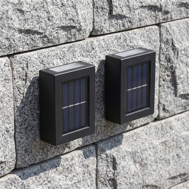 Two black compact solar up and down wall lights mounted on a textured grey stone wall in daytime.