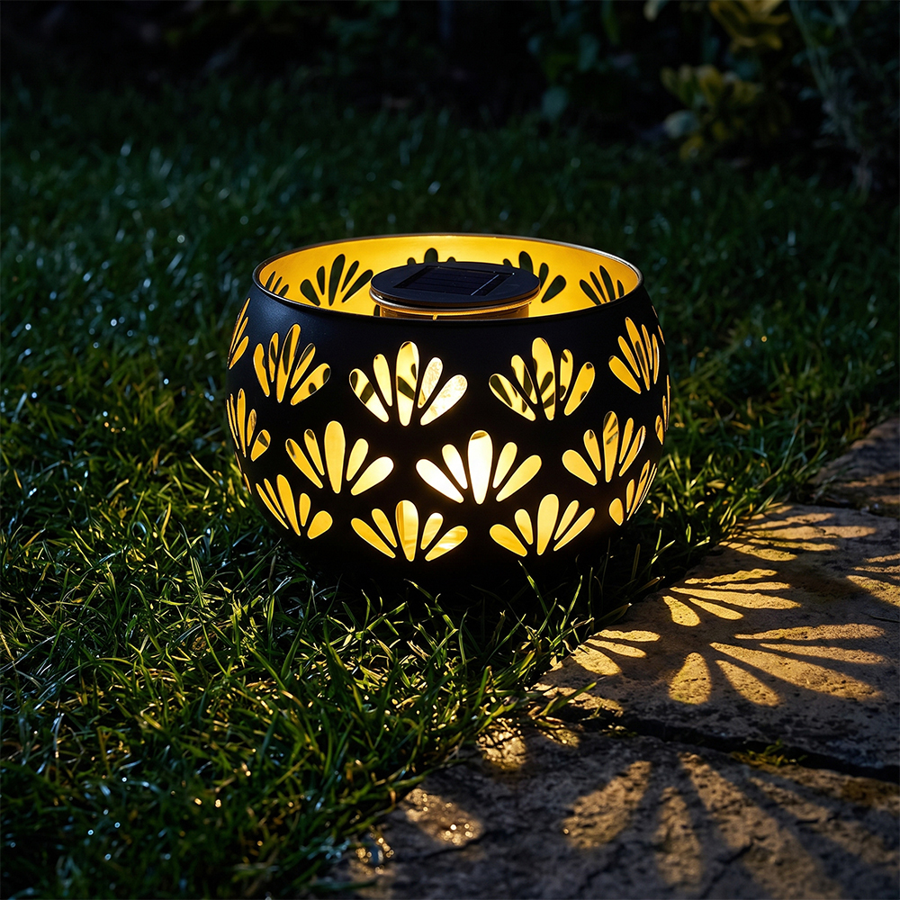 A solar garden light glowing on the grass and casting decorative fan-shaped shadow patterns at night.