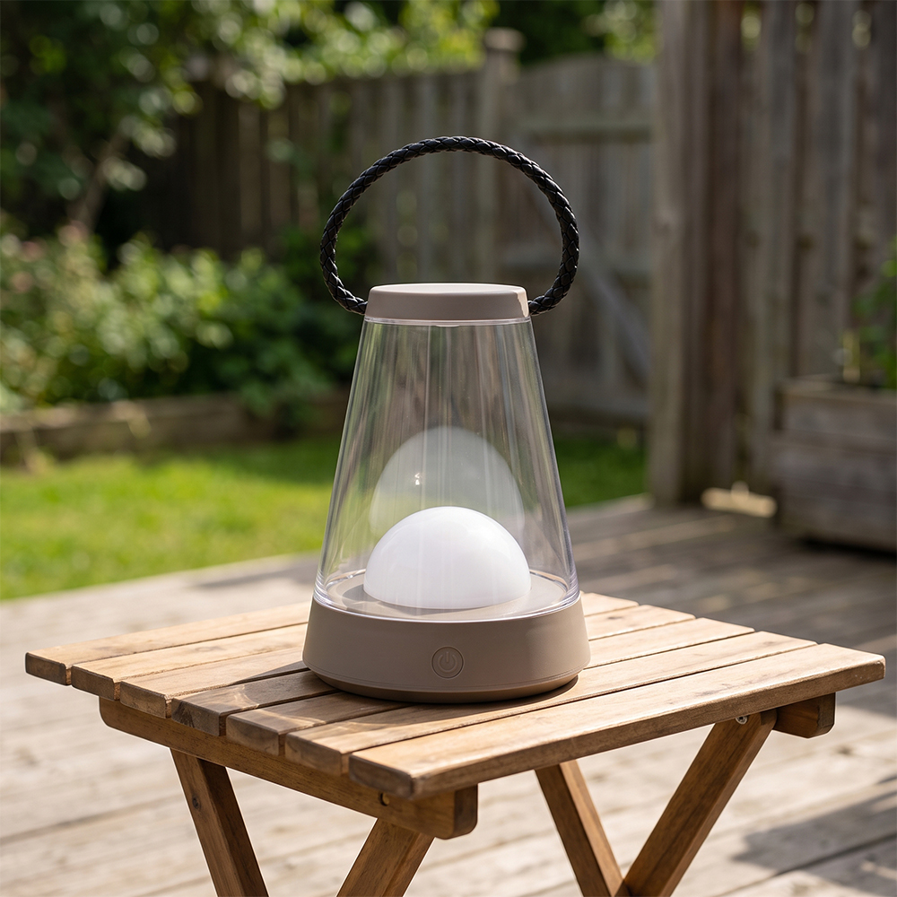 A portable LED camping lantern with a brown transparent shade and woven handle sitting on a wooden patio table.