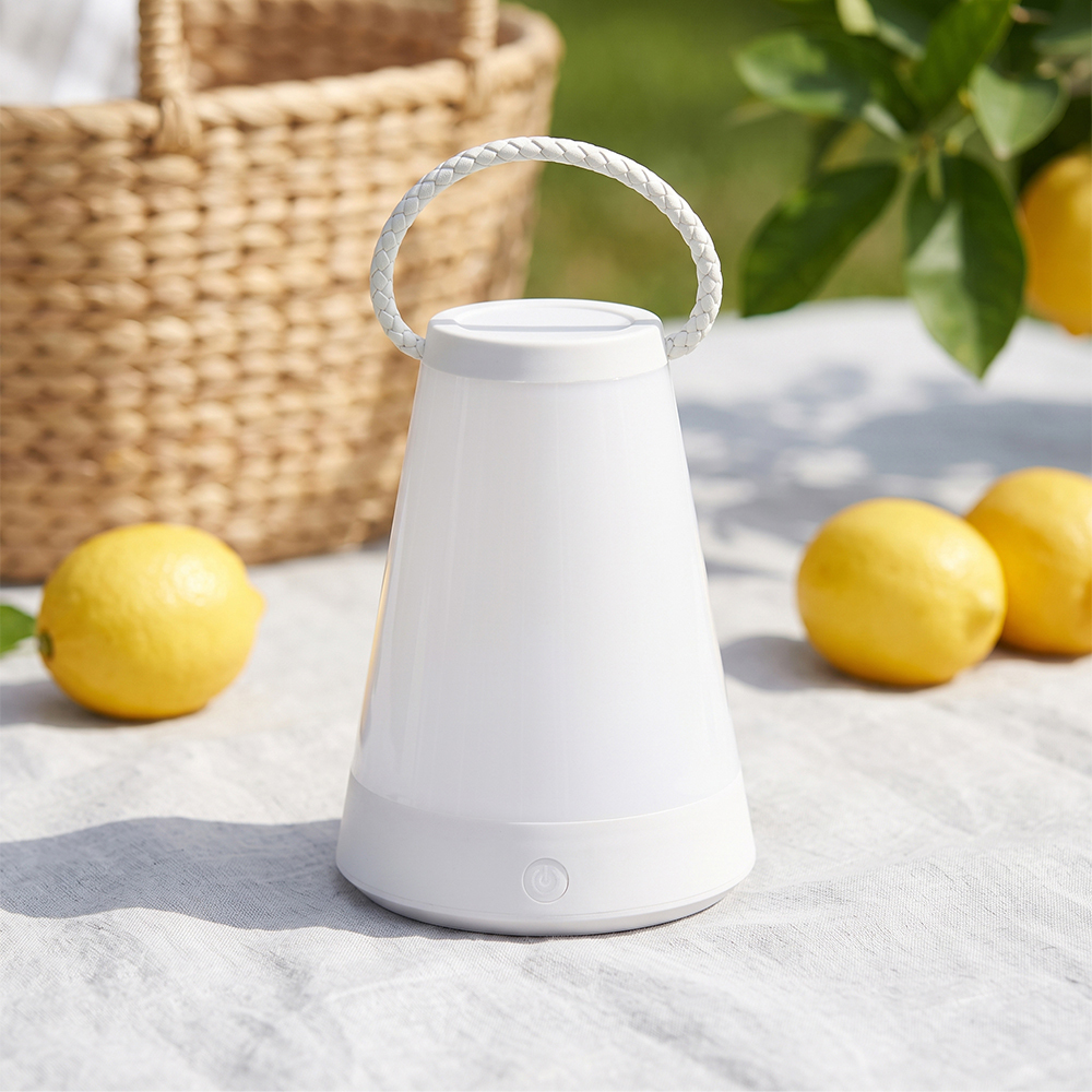 A white portable outdoor table lantern set on a picnic cloth with lemons and a wicker basket.